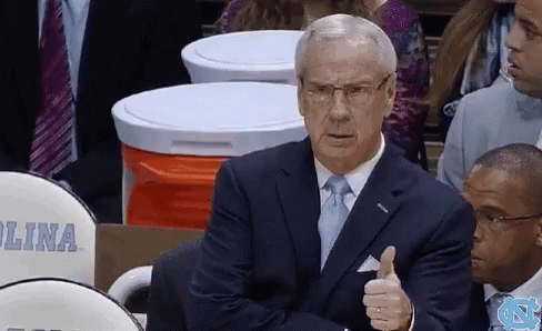 A Man In A Suit And Tie Is Giving A Thumbs Up While Sitting In The Stands GIF
