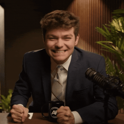 A Man In A Suit And Tie Is Giving The Middle Finger In Front Of A Microphone GIF
