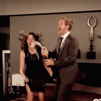 A Man In A Suit And Tie Is Holding A Bottle Of Champagne And A Woman In A Black Dress Is Holding A Feather GIF
