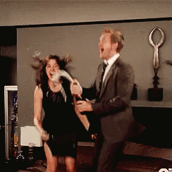 A Man In A Suit And Tie Is Holding A Bottle Of Champagne And A Woman In A Black Dress Is Laughing GIF