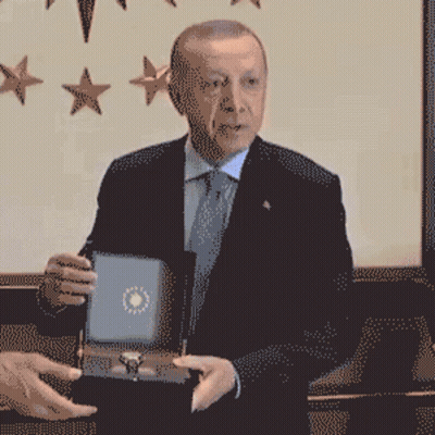 A Man In A Suit And Tie Is Holding A Box GIF