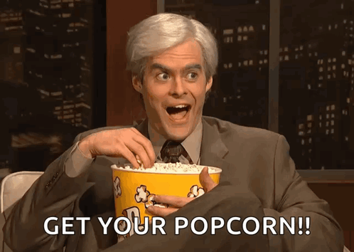 A Man In A Suit And Tie Is Holding A Bucket Of Popcorn And Saying Get Your Popcorn GIF