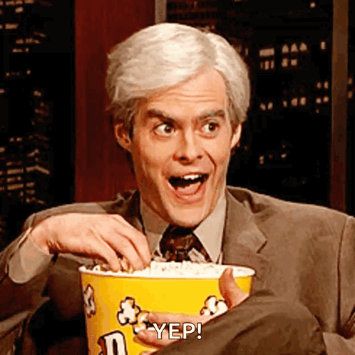 A Man In A Suit And Tie Is Holding A Bucket Of Popcorn And Says Yep GIF