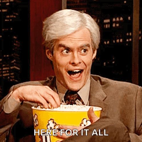 A Man In A Suit And Tie Is Holding A Bucket Of Popcorn With The Words Here For It All Below Him GIF
