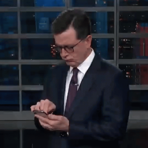 A Man In A Suit And Tie Is Holding A Cell Phone In His Hands GIF