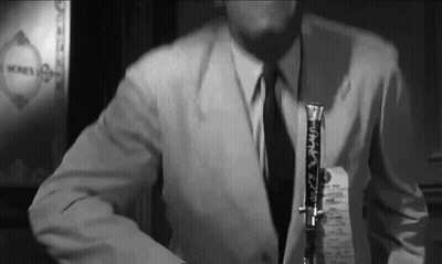 A Man In A Suit And Tie Is Holding A Clarinet GIF