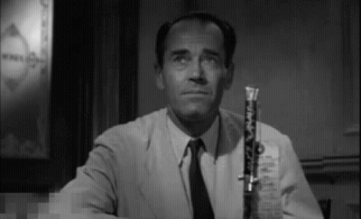 A Man In A Suit And Tie Is Holding A Clarinet In His Right Hand . GIF