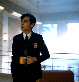 A Man In A Suit And Tie Is Holding A Cup With A Shield On His Chest GIF