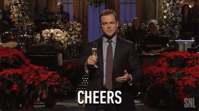 A Man In A Suit And Tie Is Holding A Glass Of Champagne And Says Cheers On The Screen GIF