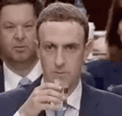 A Man In A Suit And Tie Is Holding A Glass Of Wine In Front Of A Crowd Of People . GIF