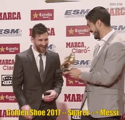 A Man In A Suit And Tie Is Holding A Golden Shoe While Another Man Looks On GIF