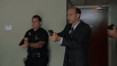 A Man In A Suit And Tie Is Holding A Gun GIF