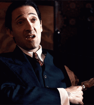 A Man In A Suit And Tie Is Holding A Gun In His Hand GIF