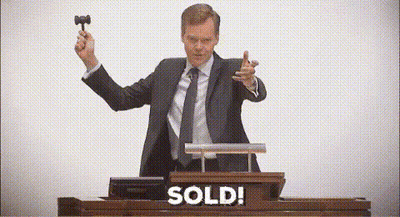 A Man In A Suit And Tie Is Holding A Hammer In Front Of A Podium That Says Sold . GIF
