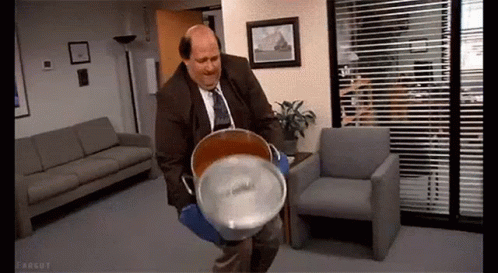 A Man In A Suit And Tie Is Holding A Large Bucket Of Water In A Waiting Room . GIF