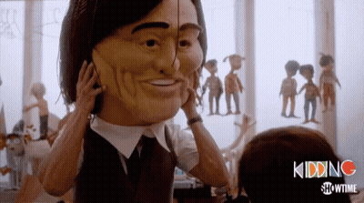 A Man In A Suit And Tie Is Holding A Large Mask On His Face GIF