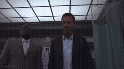 A Man In A Suit And Tie Is Holding A Large Object In Front Of A Sign That Says E. GIF