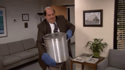 A Man In A Suit And Tie Is Holding A Large Pot In A Room . GIF