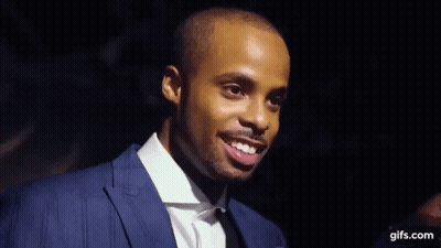 A Man In A Suit And Tie Is Holding A Microphone And Making A Face . GIF