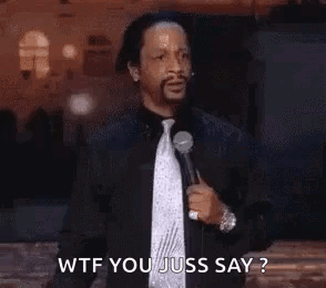 A Man In A Suit And Tie Is Holding A Microphone And Saying Wtf You Juss Say ? . GIF