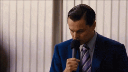 A Man In A Suit And Tie Is Holding A Microphone In His Hand GIF