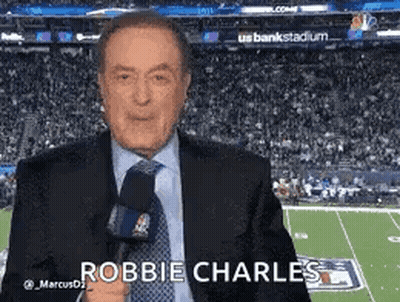 A Man In A Suit And Tie Is Holding A Microphone While Standing In Front Of A Football Field . GIF