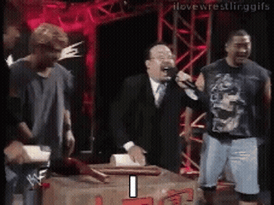 A Man In A Suit And Tie Is Holding A Microphone While Standing Next To A Box . GIF