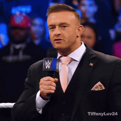 A Man In A Suit And Tie Is Holding A Microphone With A Wwe Logo On It GIF