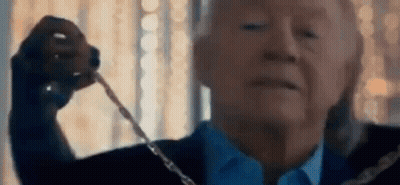 A Man In A Suit And Tie Is Holding A Necklace In His Hand . GIF