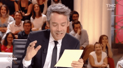 A Man In A Suit And Tie Is Holding A Piece Of Paper In Front Of A Crowd That Says Tmc On It GIF