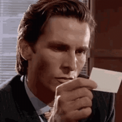 A Man In A Suit And Tie Is Holding A Piece Of Paper In Front Of His Mouth . GIF
