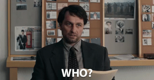 A Man In A Suit And Tie Is Holding A Piece Of Paper That Says Who GIF