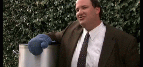 A Man In A Suit And Tie Is Holding A Pot With A Blue Oven Mitt . GIF