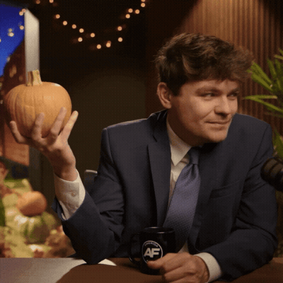 A Man In A Suit And Tie Is Holding A Pumpkin And A Coffee Mug That Says Af GIF