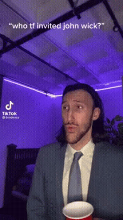 A Man In A Suit And Tie Is Holding A Red Cup And Talking About John Wick . GIF