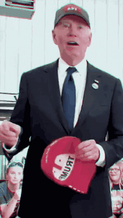 a man in a suit and tie is holding a red hat that says " i must "