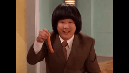 A Man In A Suit And Tie Is Holding A Sausage In His Hand And Pointing At It . GIF