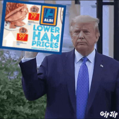 A Man In A Suit And Tie Is Holding A Sign That Says Lower Ham Prices GIF