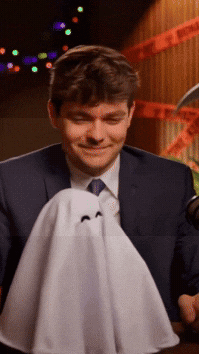 A Man In A Suit And Tie Is Holding A Small Ghost GIF