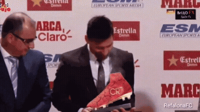 A Man In A Suit And Tie Is Holding A Soccer Boot That Says Cr7 GIF