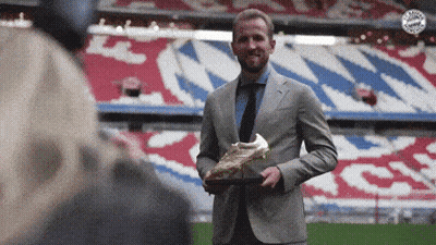 A Man In A Suit And Tie Is Holding A Soccer Boot GIF