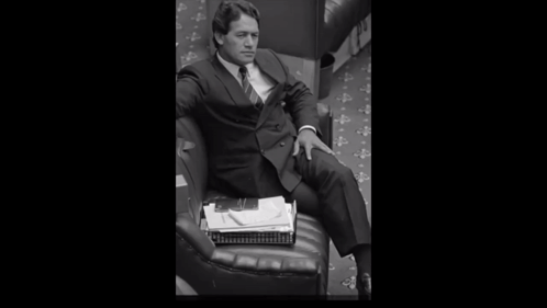 A Man In A Suit And Tie Is Holding A Stack Of Papers GIF