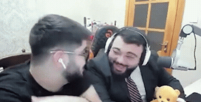 a man in a suit and tie is holding a teddy bear while sitting next to another man .