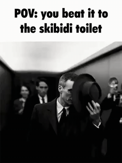 A Man In A Suit And Tie Is Holding A Top Hat In Front Of His Face While Walking Down An Elevator . GIF