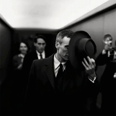 A Man In A Suit And Tie Is Holding A Top Hat Over His Face . GIF