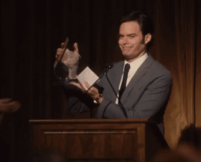 A Man In A Suit And Tie Is Holding A Trophy GIF