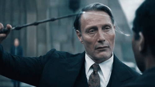 A Man In A Suit And Tie Is Holding A Wand Over His Head GIF