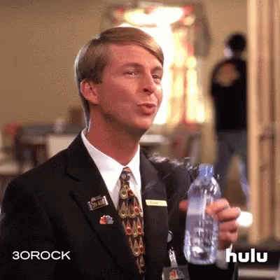 A Man In A Suit And Tie Is Holding A Water Bottle . GIF
