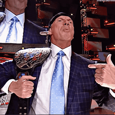 A Man In A Suit And Tie Is Holding A Wrestling Championship Belt Around His Shoulder GIF