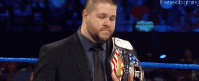 A Man In A Suit And Tie Is Holding A Wrestling Championship Belt In A Ring . GIF